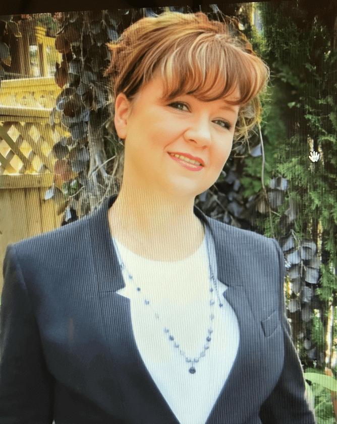 Smiling woman in a black blazer outside.
