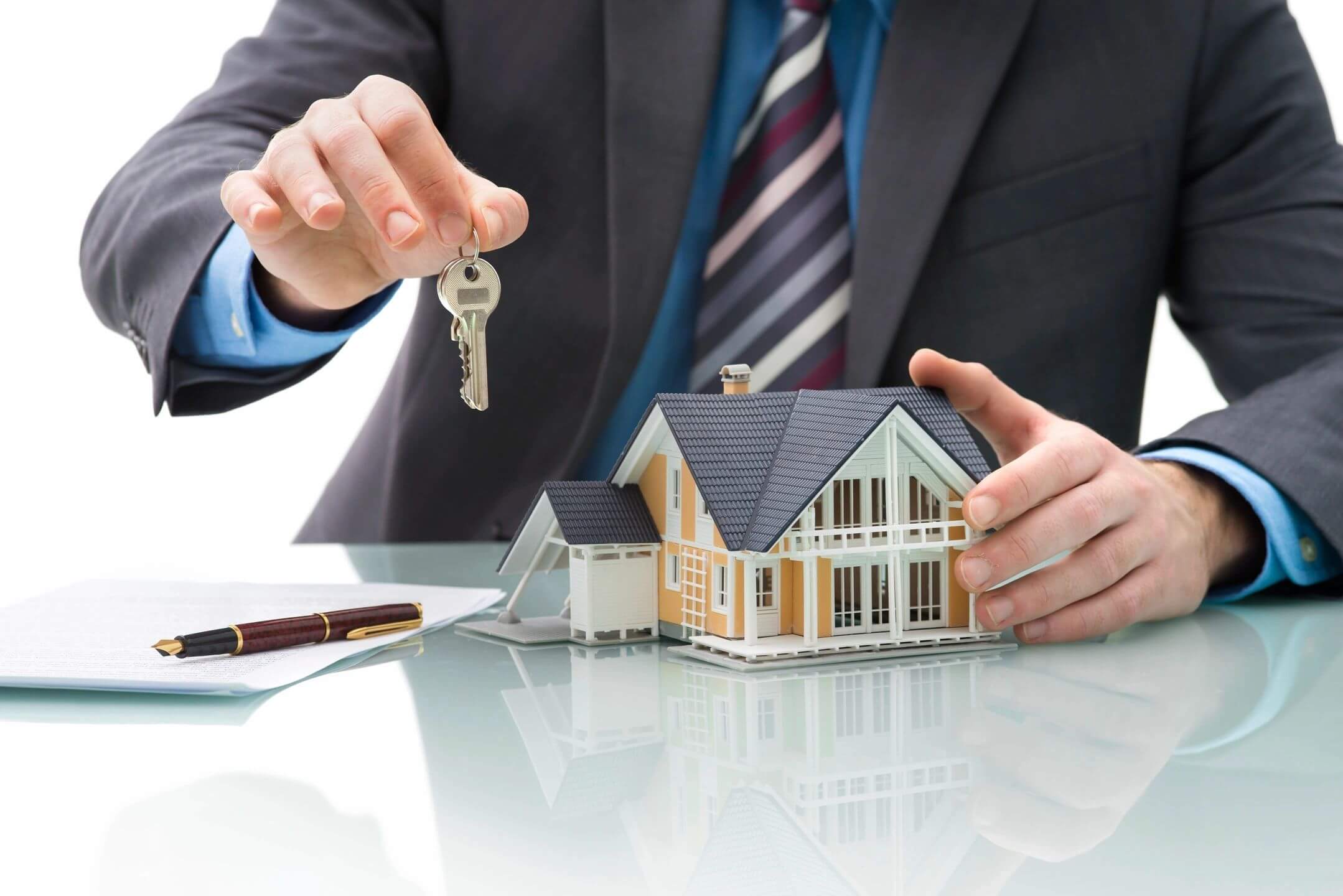 Hand holding keys over house model.